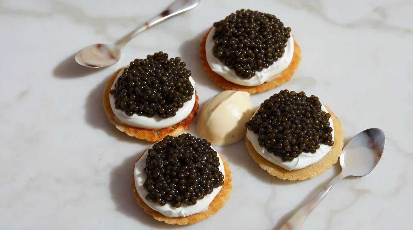 Blinis con crema y caviar sobre mármol, con dos cucharas